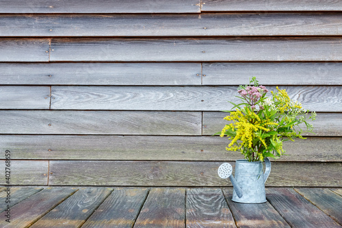 Wildflowers in a Watering Can on a Wooden Surface in Front of a Wooden Wall with Copyspace, Horizontal View 2