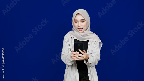 asian hijab woman wow expression see handphone isolated blue background © FAIZ