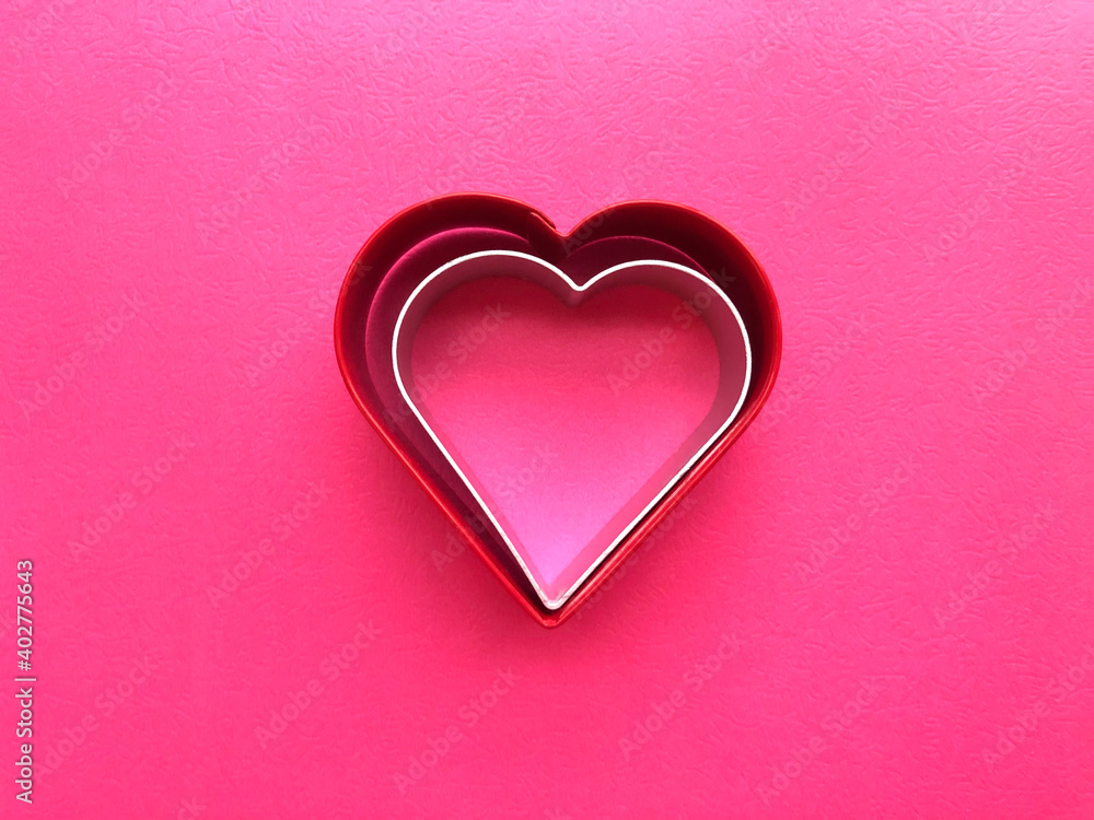 Two heart shapes -dark red and silver- within each other in the middle of hot pink background. 