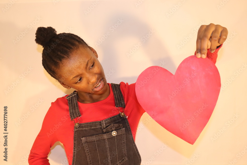 Confused girl holding up and looking at red heart sign indoors Confused girl holding up and looking at red heart sign indoors