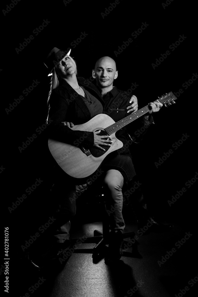 Fototapeta premium Image of a man and woman sitting in a dark room holding a guitar, creating art and music.