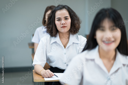 Portrait of cheerful Asian female college students writing and studying in the classroom. Selective focus teenage university students studying in classroom.
