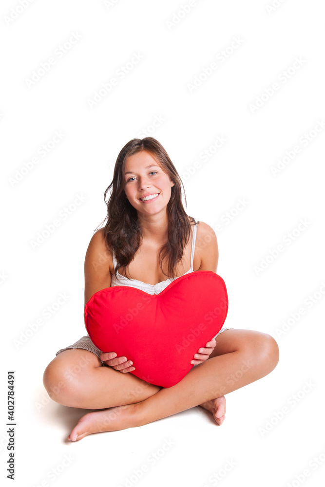 Portrait of a beautiful young woman holding a red heart pillow, isolated in front of white studio background Portrait of a beautiful young woman holding a red heart pillow, isolated in front of white studio background