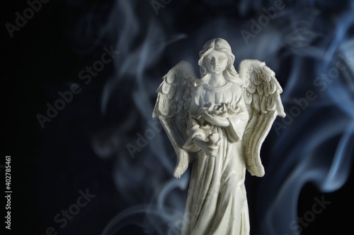 a photo of a figurine of a guardian angel surrounded by incense smoke on a black background