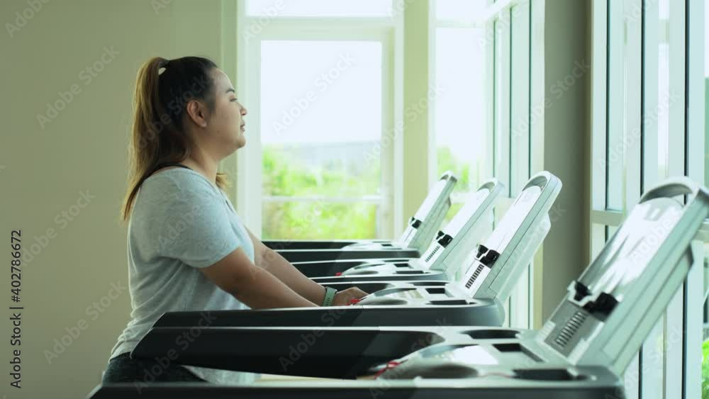 Overweight young asian woman walking on treadmill in fitness gym. Overweight young asian woman walking on treadmill in fitness gym.
