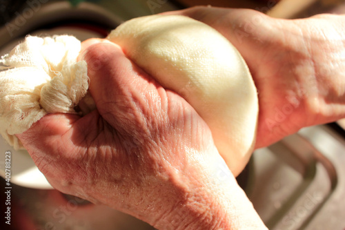 Process of making homemade ricotta cheese. Close-up of female hands with freshly made cottage cheese wrapped in cheese cloth.
