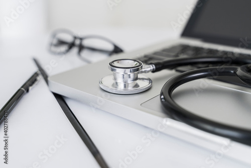 Doctor table with stethoscope, laptop, pen, clipboard and glasses for medical concept.