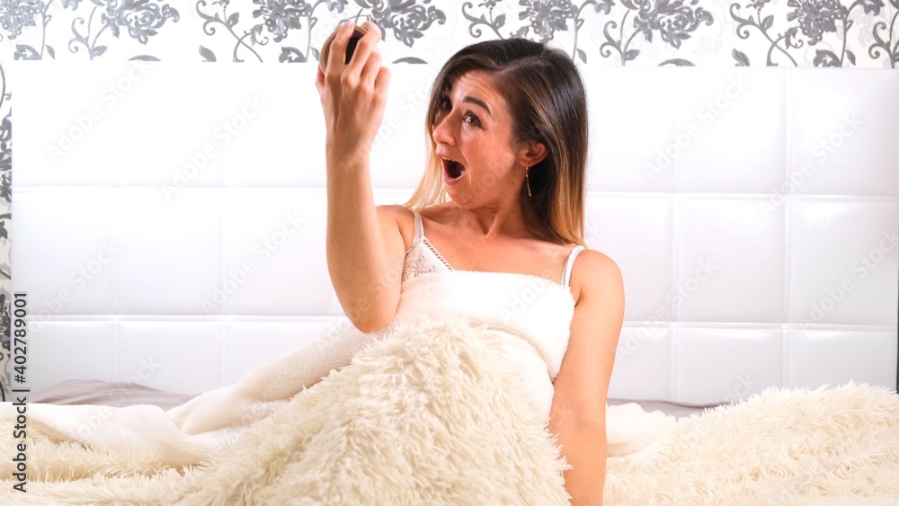 female rises in bed with an alarm clock in her hands in horror realizes that she slept. Concept of lack of time, being late for work or school female rises in bed with an alarm clock in her hands in horror realizes that she slept. Concept of lack of time, being late for work or school