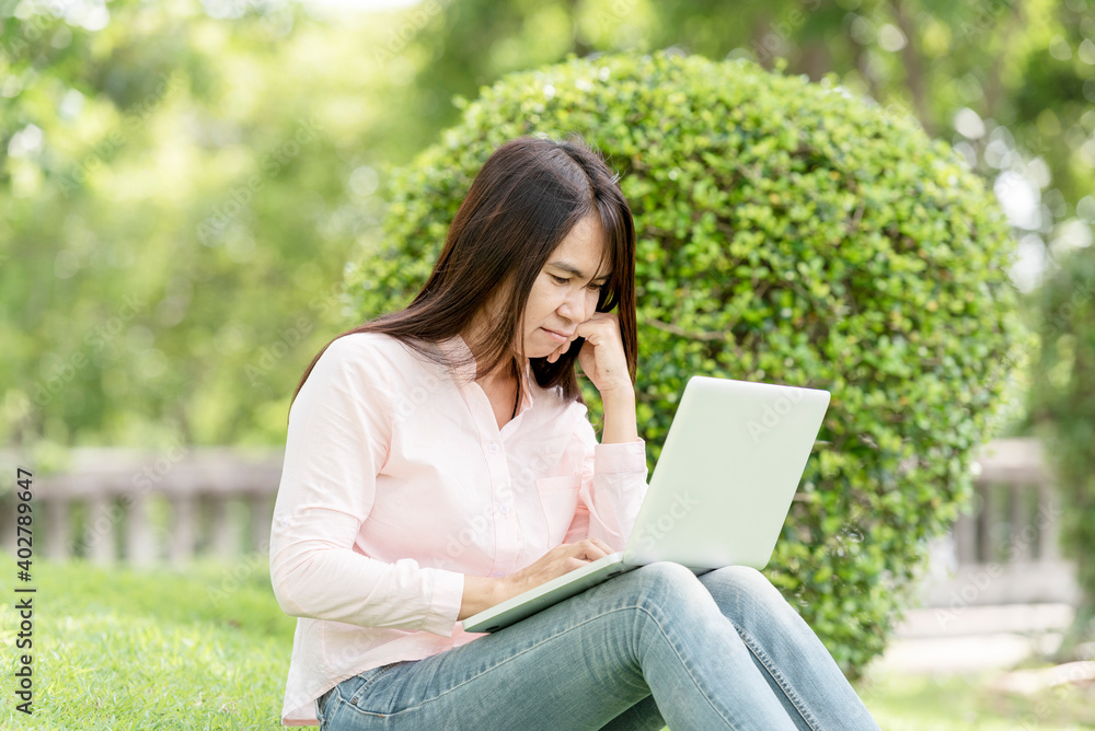 Asian woman sitting green park using laptop computer. Woman working on laptop happy entrepreneur business using notebook with hands typing on keyboard home office during coronavirus quarantine period Asian woman sitting green park using laptop computer. Woman working on laptop happy entrepreneur business using notebook with hands typing on keyboard home office during coronavirus quarantine period