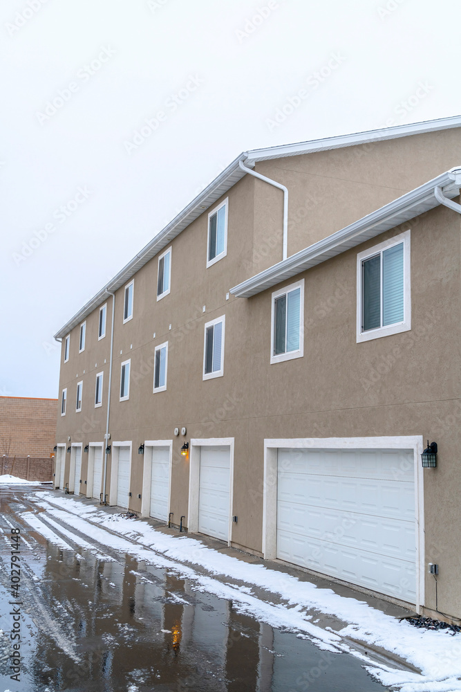 Winter on a neighborhood with wet road along white garage doors of apartments Winter on a neighborhood with wet road along white garage doors of apartments
