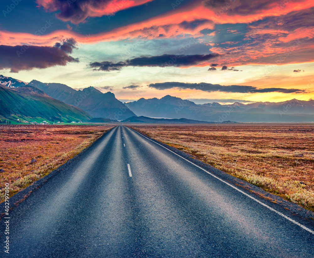 Fototapeta premium Unbelievable summer scenery. Empty asphalt road with dramatic cloudy sky. Fantastic Sunrise in Iceland. Typical icelandic landscape with volcanic hills. Traveling concept background..