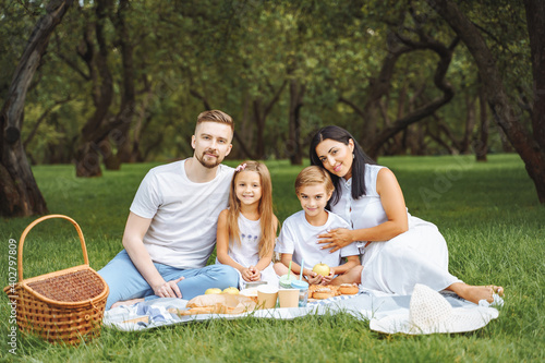 Portrait of a happy family hugging and looking at the camera while relaxing on the lawn during a picnic in a green garden