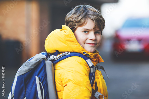 Little school kid boy of elementary class walking to school. Portrait of happy child on the street with traffic. Student with in yellow jacket and backpack in colorful winter clothes.