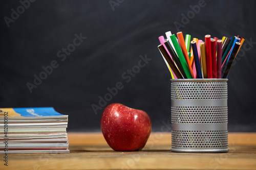red apple, books and penciles on wooden table and blackdoard background.school for kids.