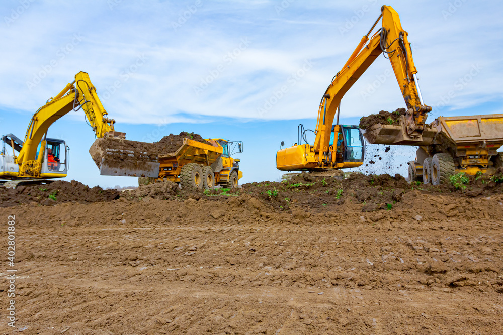 Big excavators are loading two trucks with ground on building site Big excavators are loading two trucks with ground on building site