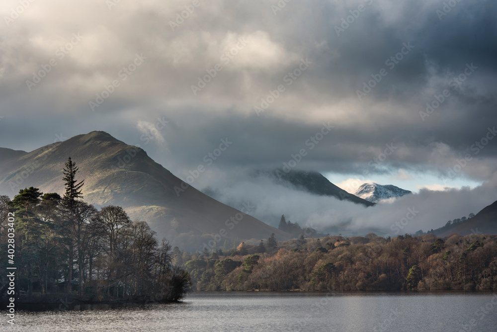 Fototapeta premium Dramatic landscape image looking across Derwentwater in Lake District towards Catbells snowcapped mountain with thick fog rolling through valley
