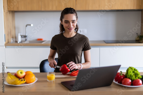 Young woman enjoying cooking looking for a recipe on the laptop in the kitchen