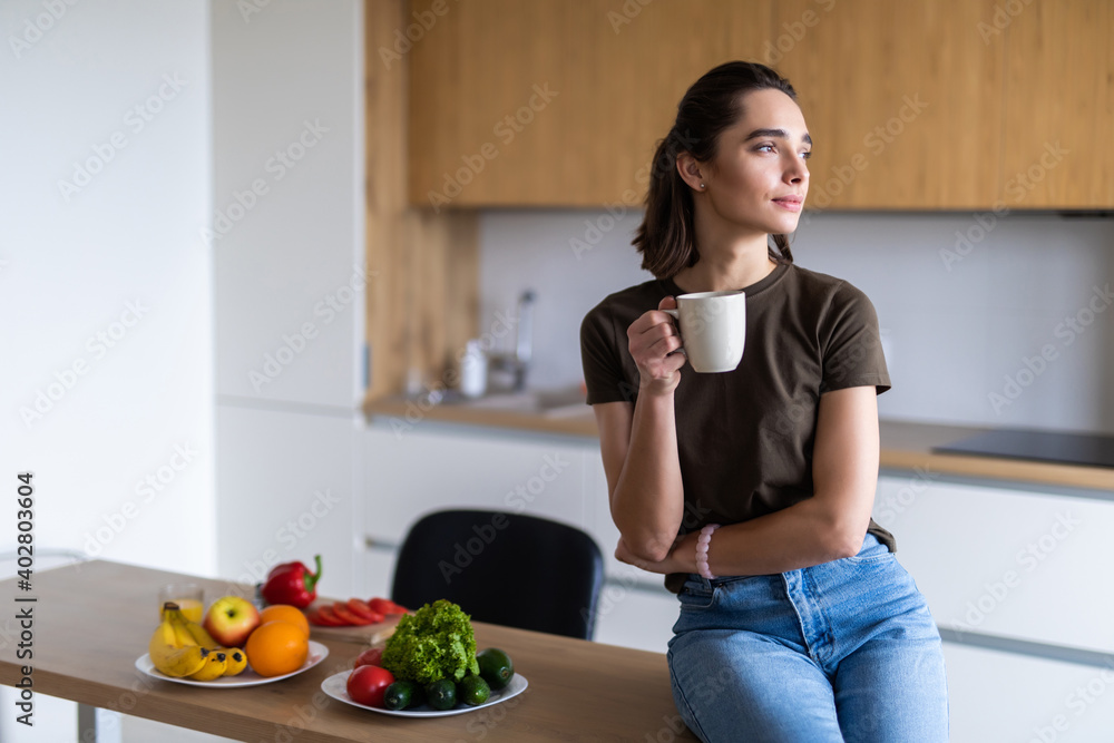 Young woman cook table while having a drink from a cup in the kitchen Young woman cook table while having a drink from a cup in the kitchen