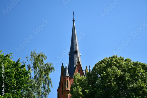 Eine Backstein Kirchspitze mit Bäumen und blauem Himmel