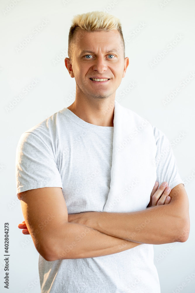 Athletic man portrait. Healthy lifestyle. Sport recreation. Vertical portrait of confident cheerful spa massage therapist in white t-shirt with towel on shoulder isolated on light background. Athletic man portrait. Healthy lifestyle. Sport recreation. Vertical portrait of confident cheerful spa massage therapist in white t-shirt with towel on shoulder isolated on light background.