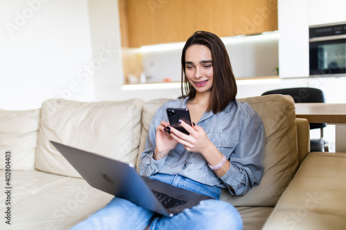 Young woman working with a laptop and mobile phone sitting on a couch at home