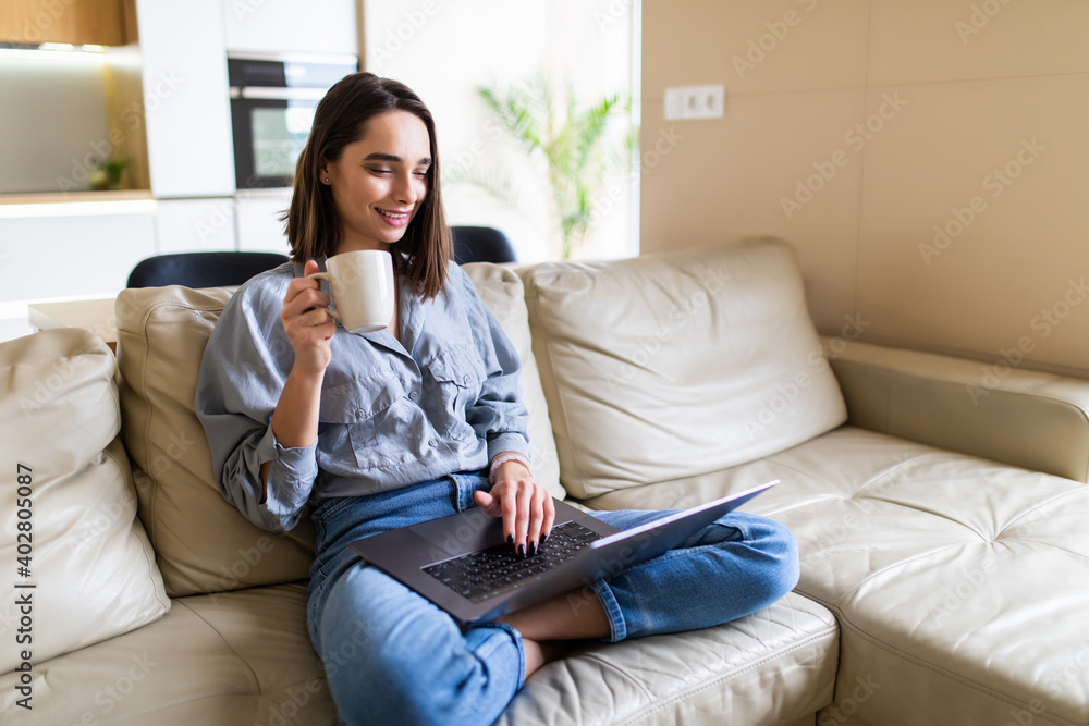 Young woman drinking a coffee and using her laptop in the living room. Working from home in quarantine lockdown. Social distancing Self Isolation Young woman drinking a coffee and using her laptop in the living room. Working from home in quarantine lockdown. Social distancing Self Isolation
