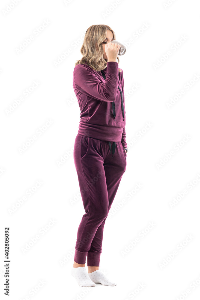 Side view of young woman in comfy home clothing drinking coffee or tea. Full body length isolated on white background. Side view of young woman in comfy home clothing drinking coffee or tea. Full body length isolated on white background.