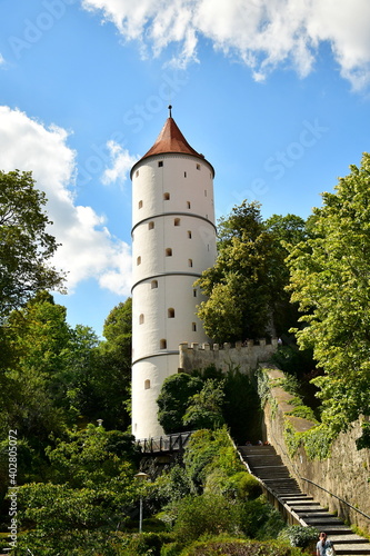 Ein weißer Turm samt Stadtmauer zwischen alten Bäumen und einer Treppe