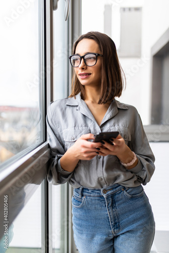 Canvastavla Excited beautiful woman in eyeglasses using smartphone while sitting near window