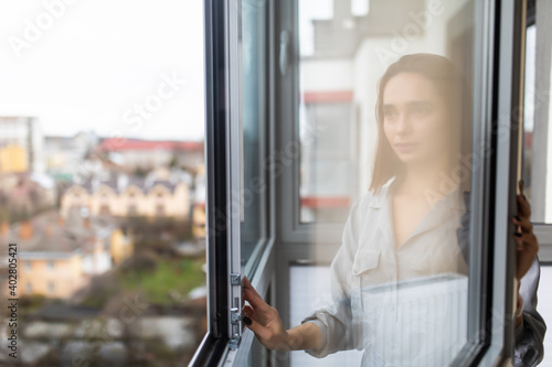 Young woman opening window in living room at home