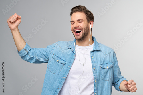 Close up portrait of cheerful young man enjoying listening to music wearing casual jeans outfit