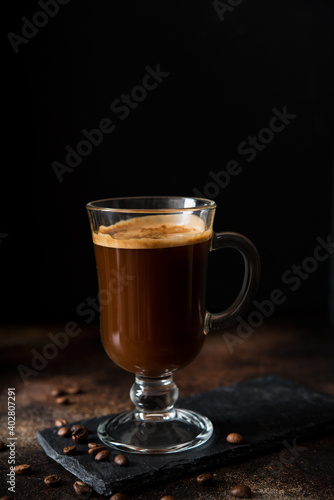 Black hot arabica coffee with foam in a glass glass on a dark