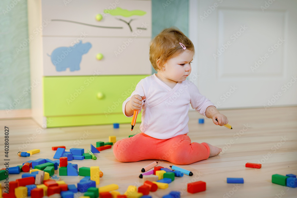 Cute little baby girl playing with educational toys. Happy healthy child having fun with colorful different wooden blocks at home or nursery. Baby crawling and learning colors and forms, indoors Cute little baby girl playing with educational toys. Happy healthy child having fun with colorful different wooden blocks at home or nursery. Baby crawling and learning colors and forms, indoors