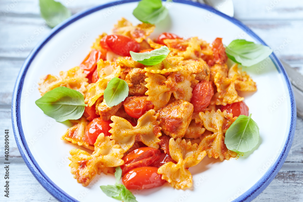Farfalle pasta with chicken breast, cherry tomatoes and fresh basil. Bright wooden background. Close up. 
