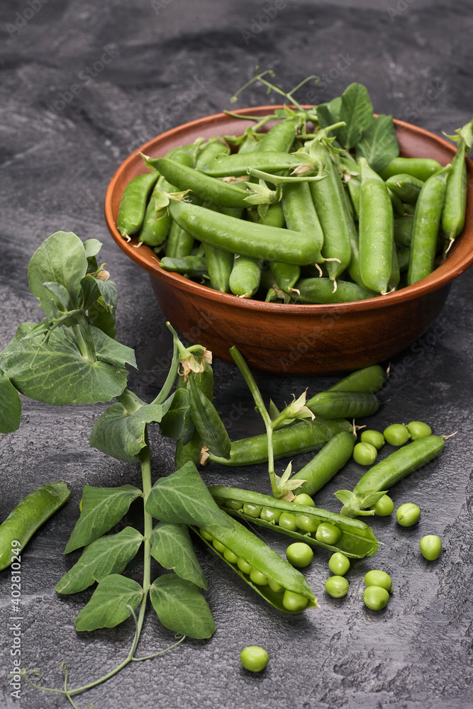 Pods of green peas with leaves in bowl on grey loft background Pods of green peas with leaves in bowl on grey loft background