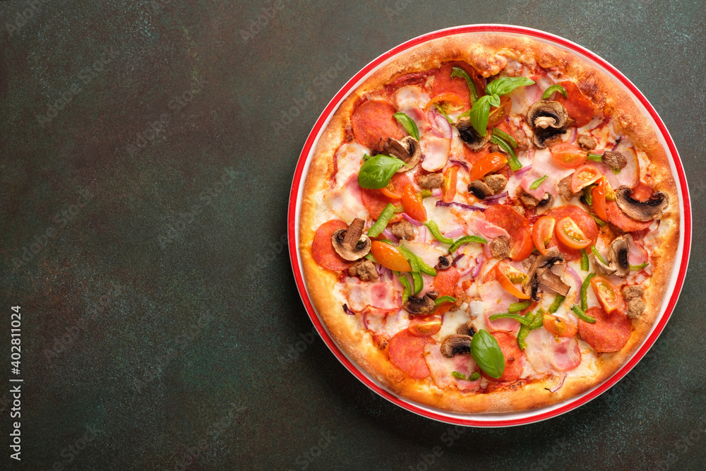 Pizza with bacon, spicy pepperoni, mozzarella, cherry tomatoes, mushrooms, red onion and sweet pepper on a dark green background. Copy space, top view.