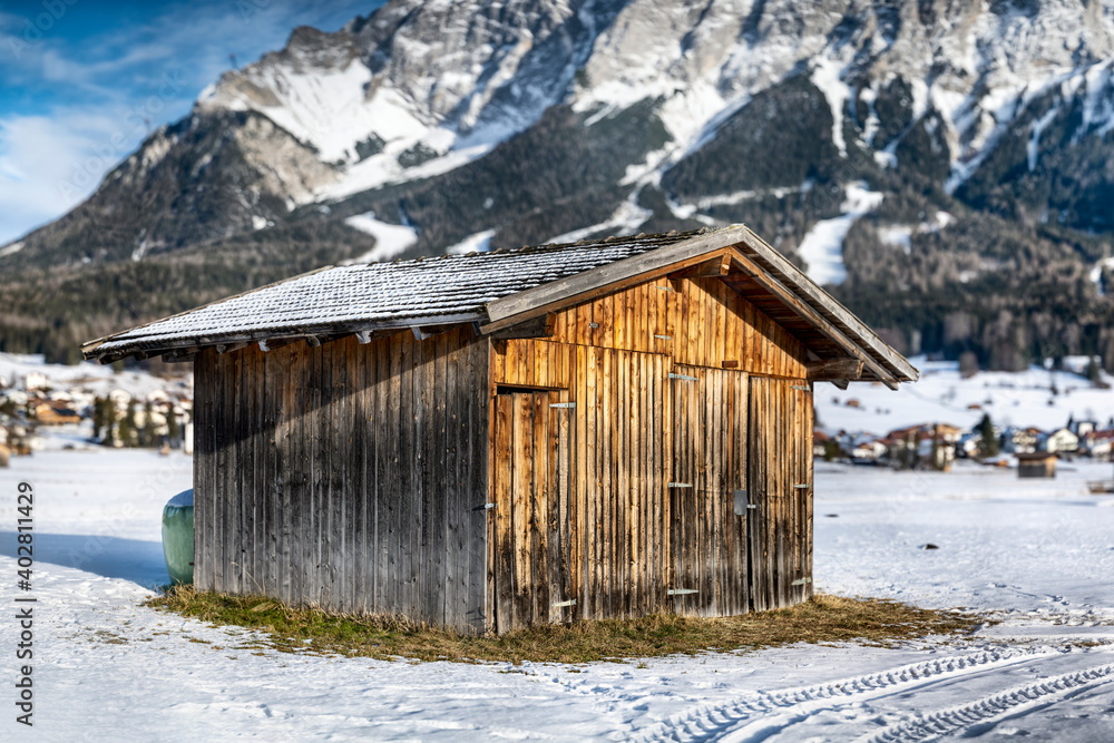 old equipment barn with sunburned wood in a snow-covered field in front of the Zugspitze mountain
