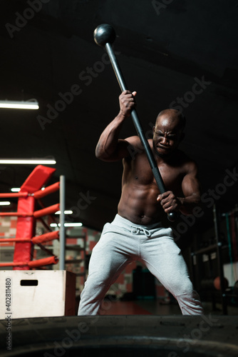 A male with a naked torso works out in a simulator with a hammer and prepares to hit © DmitryStock