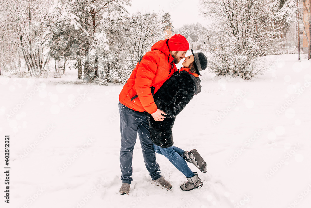 Young romantic couple is having fun outdoors in winter. Snowing. Love and leisure concept. Enjoying spending time together. Two lovers are hugging and kissing in Saint Valentine's 