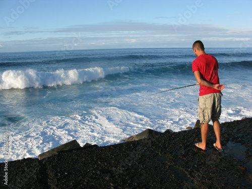 Pêcheur à la ligne sur des rochers devant une vague © Christophe Rubin