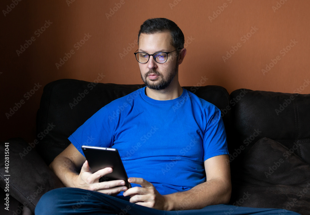 Happy man in glasses use tablet computer, sitting on sofa at home. Happy man in glasses use tablet computer, sitting on sofa at home.