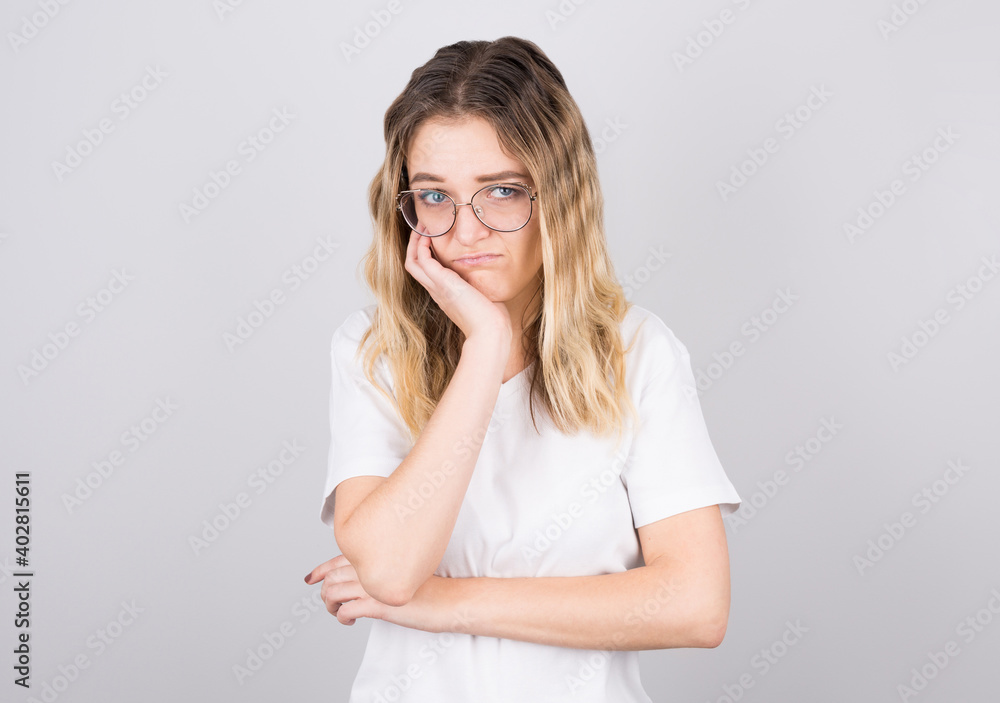 pretty girl in black glasses touching her face and bending over, peeking out from under her eyes, hating talking to a boring person, standing against a gray background pretty girl in black glasses touching her face and bending over, peeking out from under her eyes, hating talking to a boring person, standing against a gray background