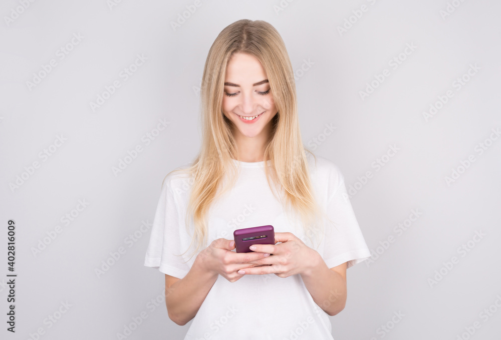 Excited young woman looking at her mobile phone smiling. Woman reading text message on her phone, isolated over white background. Excited young woman looking at her mobile phone smiling. Woman reading text message on her phone, isolated over white background.