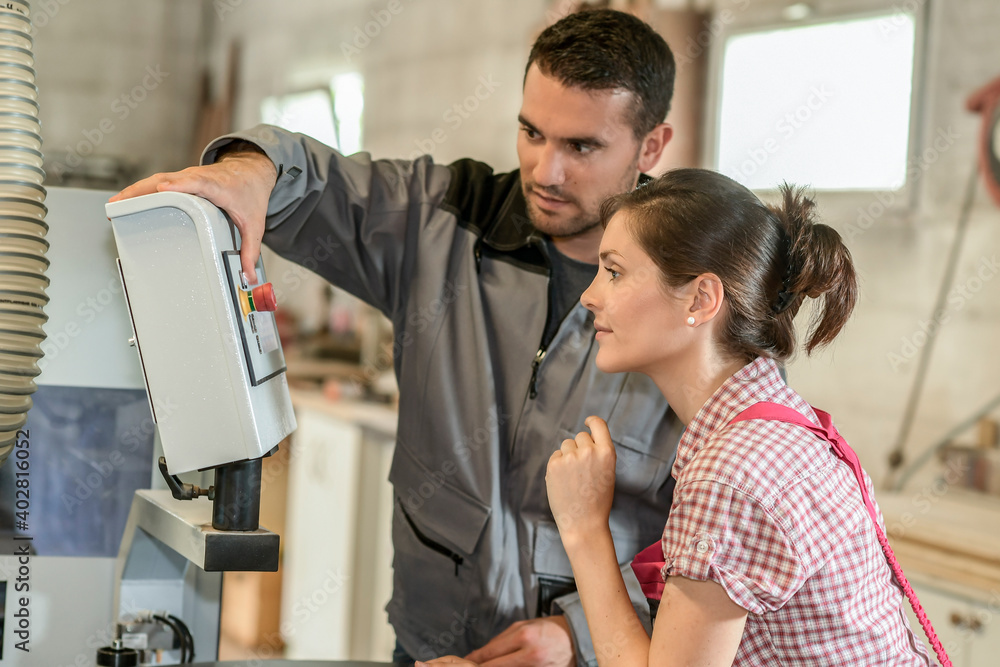 Male worker teaching female apprentice how to operate a machine Male worker teaching female apprentice how to operate a machine