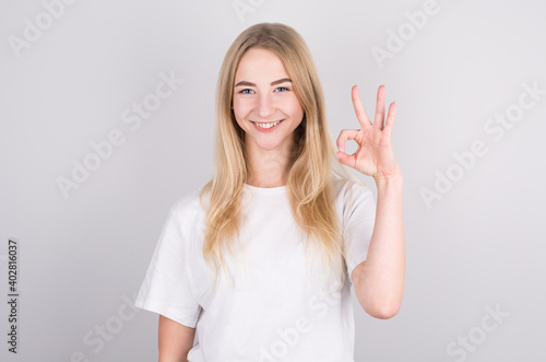 Girl with long, white hair smiling and showing ok sign on white background.