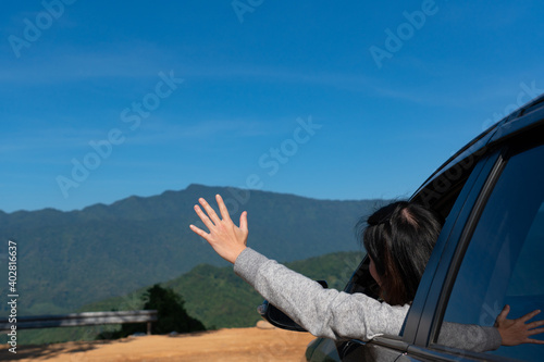young woman heading out of car and waving hand to enjoy beautiful of mountain during vacation