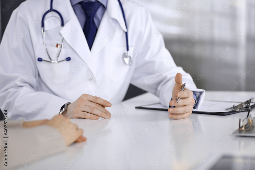 Unknown male doctor and patient woman discussing something while sitting in clinic and using clipboard. Best medical service in hospital, medicine, pandemic stop Unknown male doctor and patient woman discussing something while sitting in clinic and using clipboard. Best medical service in hospital, medicine, pandemic stop