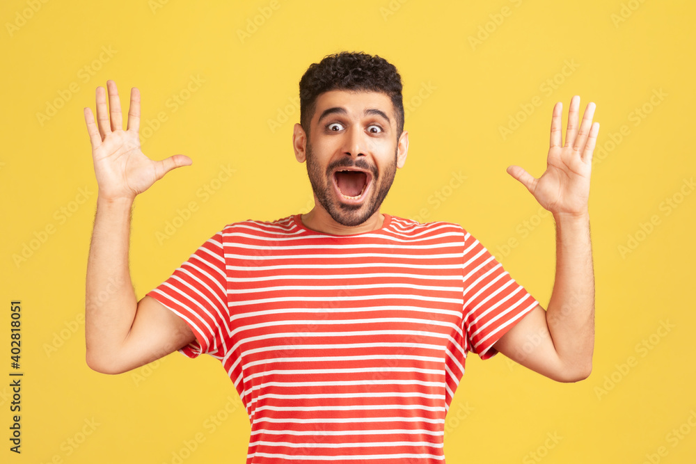 Shocked surprised bearded man in red striped t-shirt looking at camera with big eyes and widely opened mouth, amazed and excited. Indoor studio shot isolated on yellow background Shocked surprised bearded man in red striped t-shirt looking at camera with big eyes and widely opened mouth, amazed and excited. Indoor studio shot isolated on yellow background