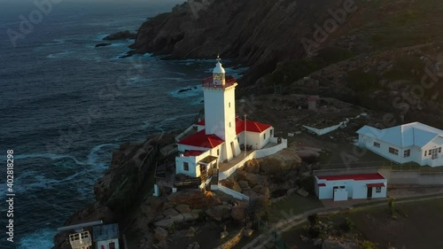 Drone shot of a Red lighthouse on the edge of a cliff overlooking the sea. photo