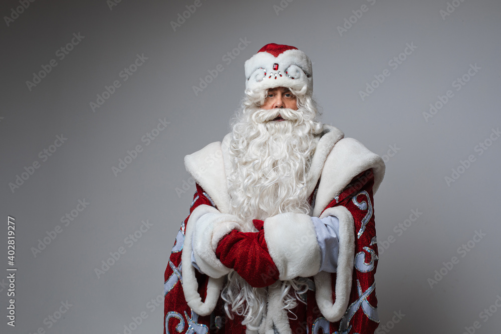 Portrait of emotionless Father Frost with long white beard wearing traditional costume holding hands together and looking at camera with calmness. Ready to give a speech.